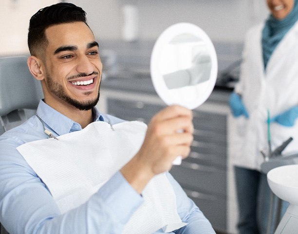 Man smiling at reflection in handheld mirror