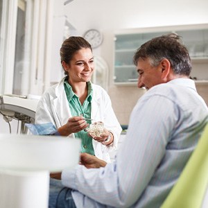 Smiling dentist showing patient model of teeth