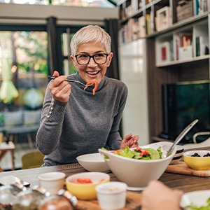Woman with black glasses smiling while eating with friend