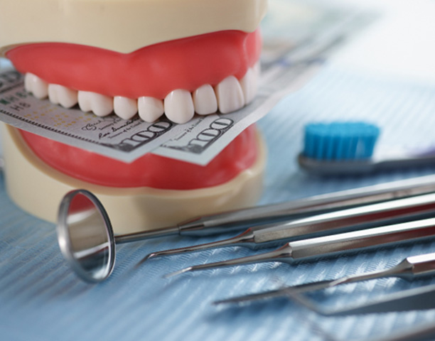An artificial jaw mockup biting hundred-dollar bills next to dental tools