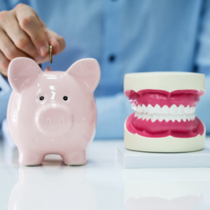A person inserting a coin into a piggy bank next to a jaw mockup