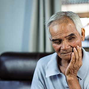 Older man on couch touching jaw and looking concerned