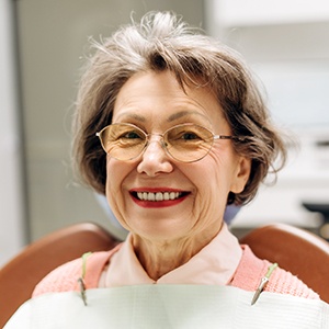 Older woman with glasses sitting in dental chair and smiling