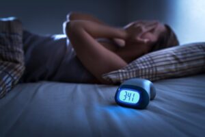 A sleepless person with an alarm clock in the foreground.